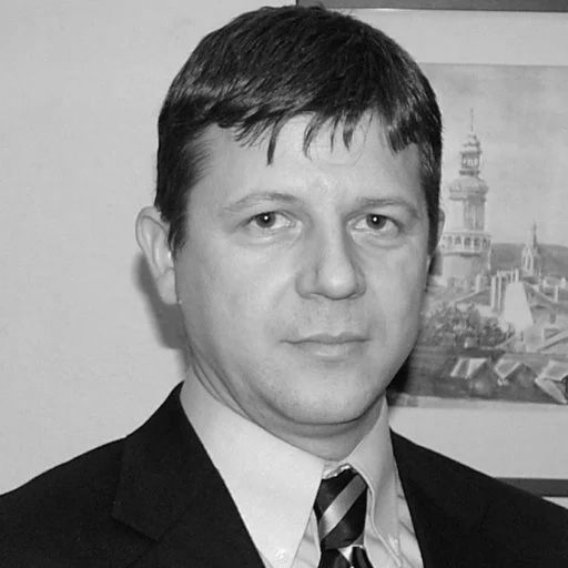 Black and white photo of man in suit and tie stands in front of picture hanging on wall.