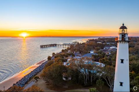 Picture of sunset over a beach and boardwalk by a lighthouse.