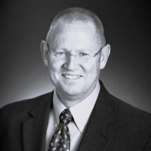 Black and white photo of person wearing glasses, tie, and jacket.