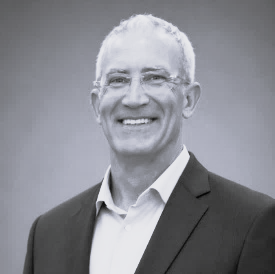 Black and white picture of person wearing glasses and button up with blazer.