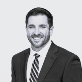 Photo shows black and white headshot person in suit and tie in front of a white background.